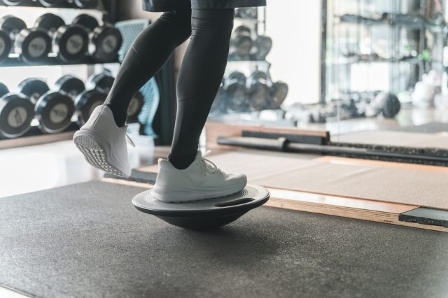 Frau balanciert auf einem Trainingsgerät und trainiert ihr Gleichgewicht