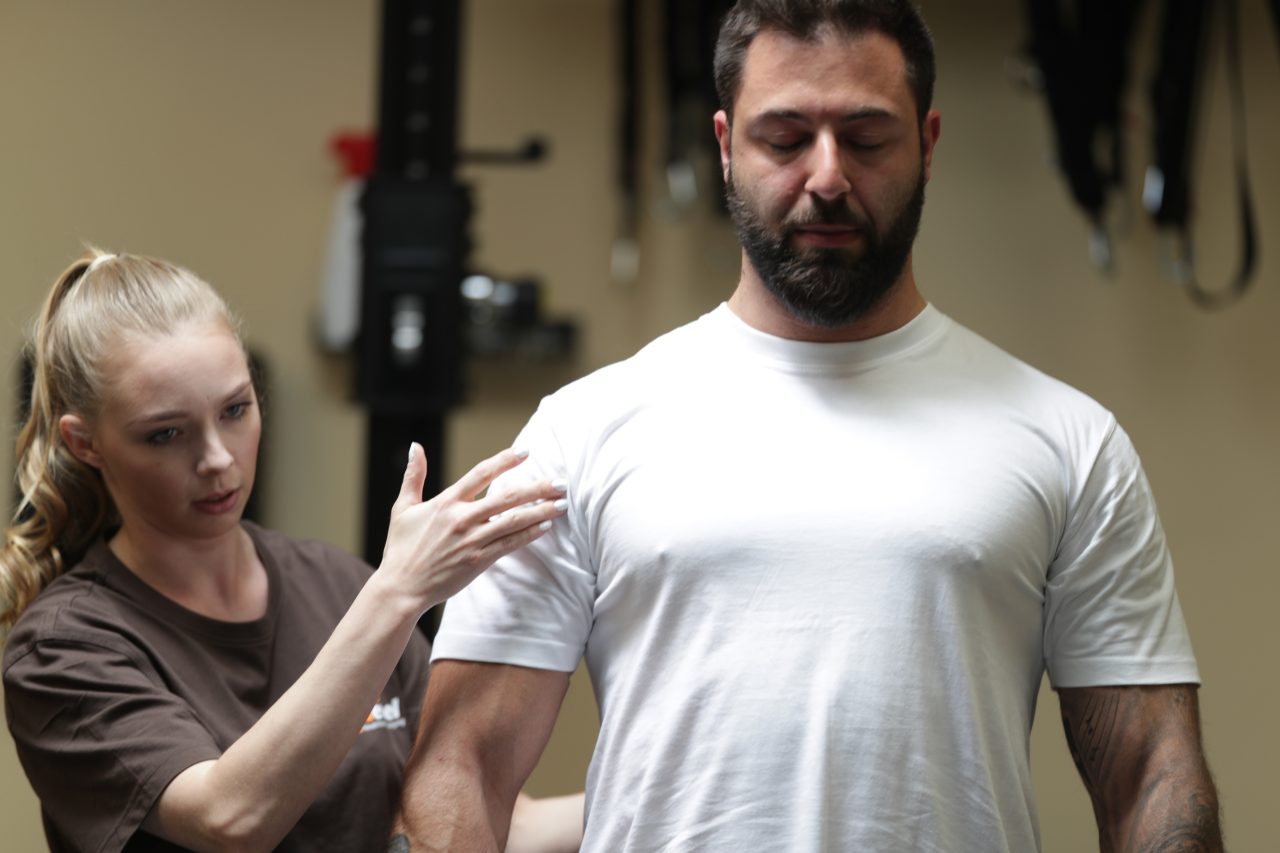 Physiotherapeutin behandelt die Schulter eines Mannes mit manueller Therapie zur Schmerzlinderung.